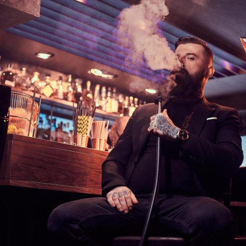 portrait-tattooed-bearded-man-which-is-smoking-hookah-making-nice-vapour-while-sitting-near-bar-counter